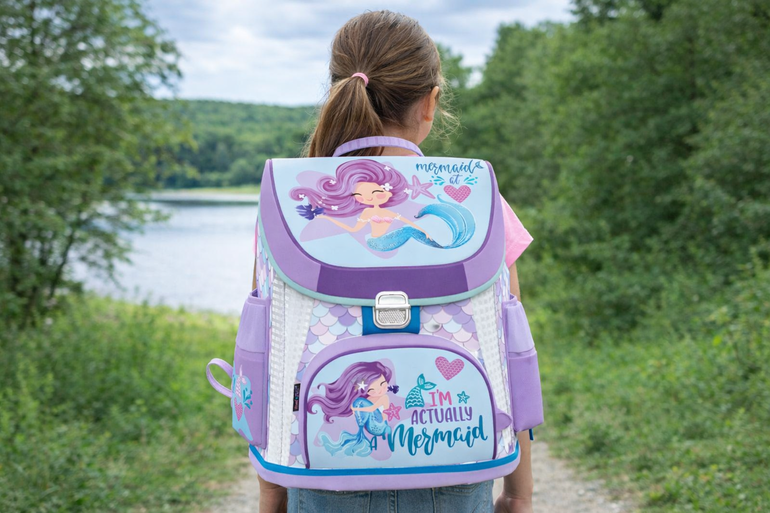 Момиче на природен фон с ученическа раница с дизайн русалка в лилаво и тюркоазено, предлагана от Книжарница Първолаче